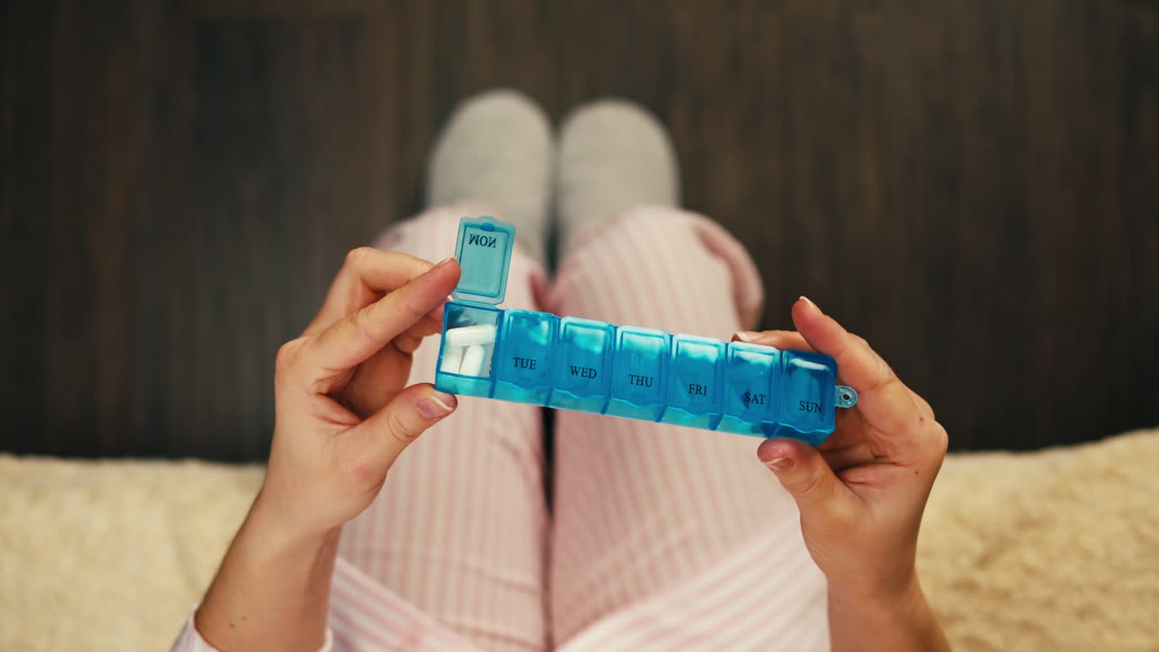 mujer tomando pastillas de un organizador de pastillas semanales