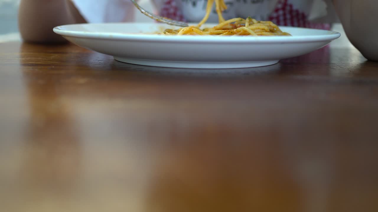 A little girl eats tomato seafood spaghetti in a restaurant. The foreground is blurred and the focus is on the back. The subject is in the middle of the screen.