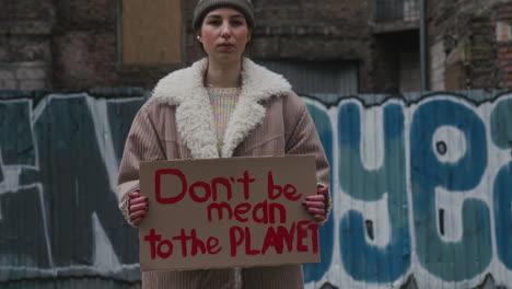 young girl looking at camera and holding a cardboard placard with the phase dont be mean the planet during a climate change protest