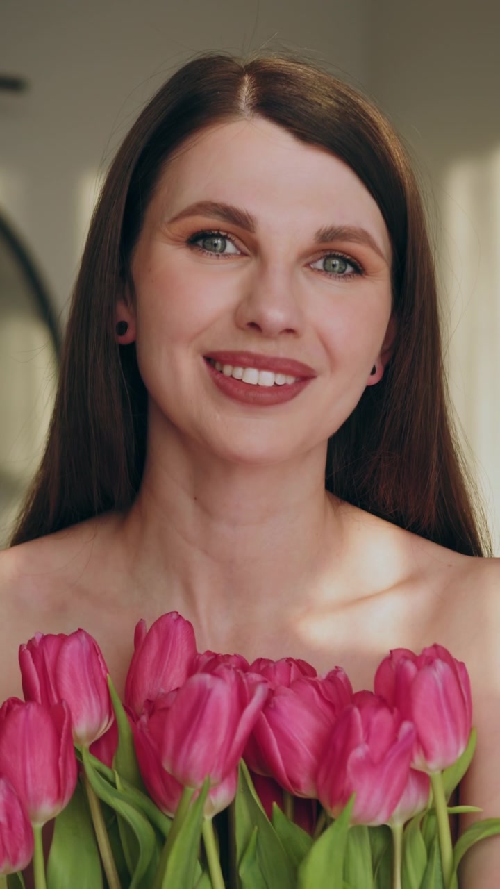 Giovane donna con lunghi capelli castani sorride, tenendo un bouquet di tulipani rosa vivaci, trasmettendo gioia e