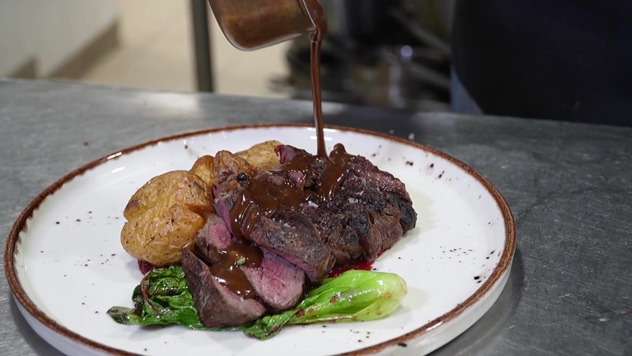 Chef che versa salsa di riduzione su filetto al sangue e patate arrosto