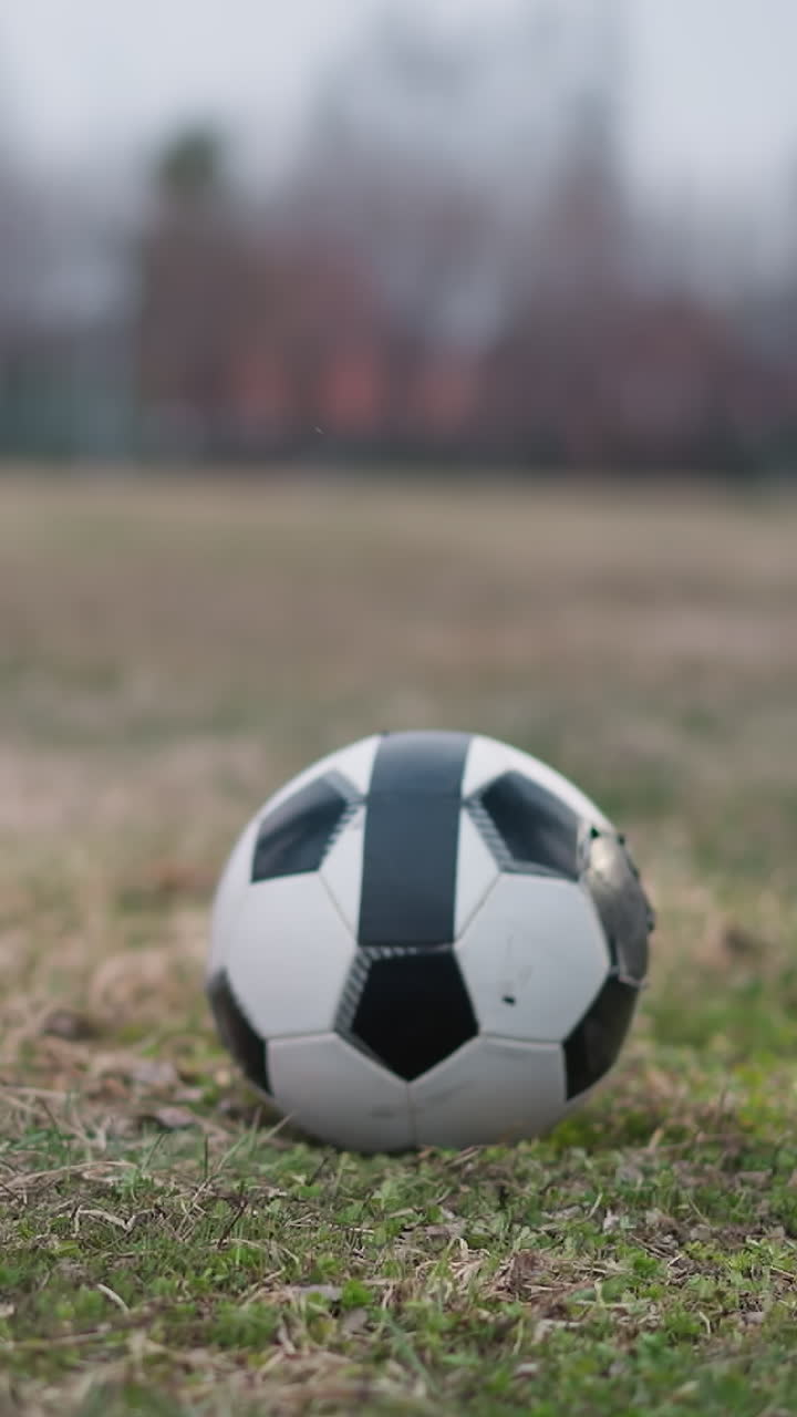 Close-up leg view of two people preparing to play soccer with a ball placed between them on a grassy field, the background is blurred, showcasing a football post in the distance