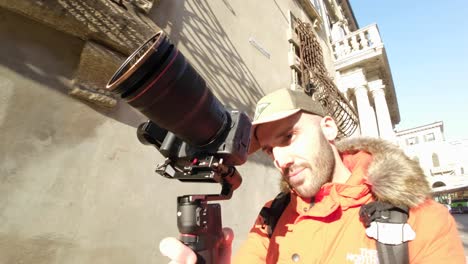 man walking along city street while holding professional camera mounted on stabilizing gimbal dji rs3 mini