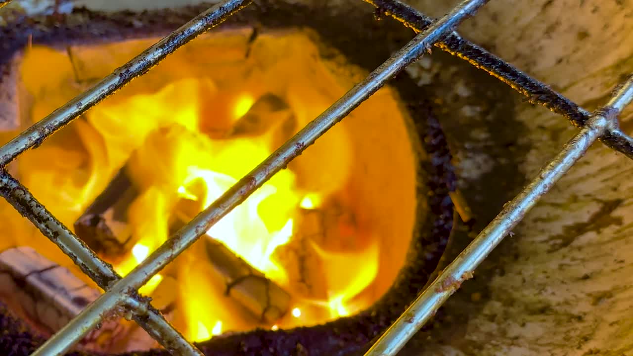 Intense flames flicker through a metal grate, showcasing the vibrant energy of burning charcoal.