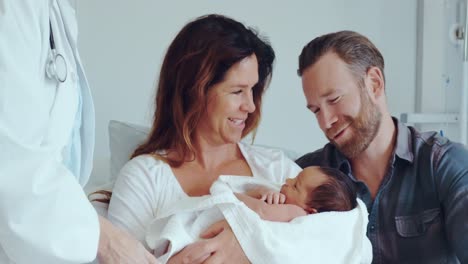 Front-view-of-Caucasian-couple-with-doctor-holding-their-newborn-baby-in-the-ward-at-hospital