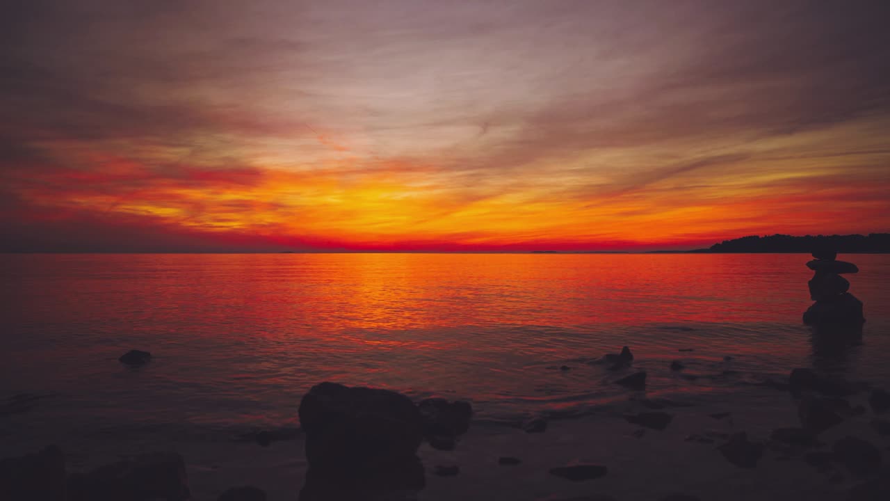 Time lapse of the sun setting over the horizon at a scenic natural romantic calm water beach with small waves at the Croatian Mediterranean seaside as a big, orange ball. Outdoors tourism vacation sunset cinemagraph seamless video loop im 4K UHD.