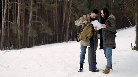 caucasian couple checking map for directions in a snowed forest.