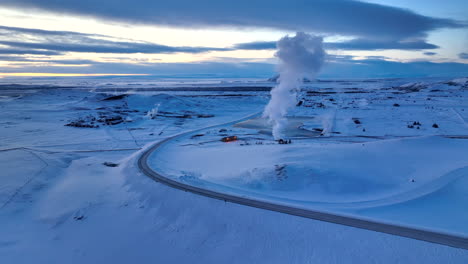 Drohnenschwenk-Auf-Der-Hochland-Myvatn-Straße-Durch-Heißen-Weißen-Dampf,-Der-Von-Geothermischen-Anlagen-In-Der-Weißen,-Schneebedeckten-Isländischen-Landschaft-Kommt