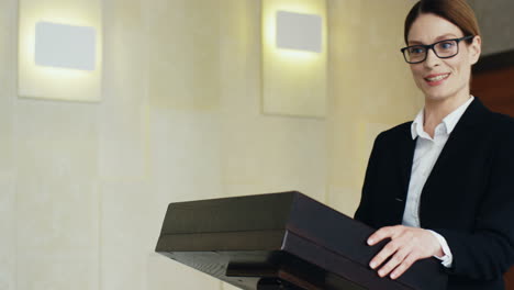 회의에서 빈 연단, 안경을 쓴 젊은 백인 여성 사업가가 다가와 연설을 시작합니다.