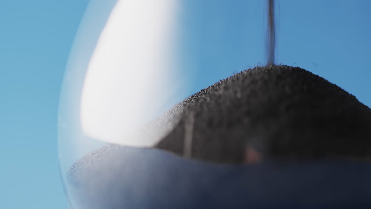 파란색 배경에 복사 공간과 함께 흘러내리는 검은 모래와 함께 모래시계의 클로즈업 비디오