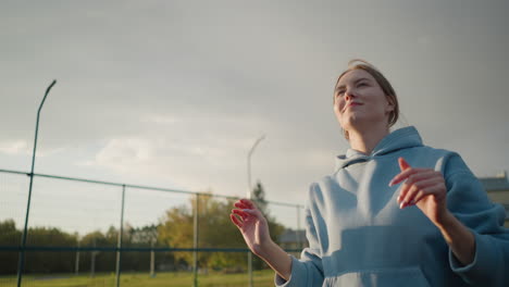 lady in green sweater playing volleyball outdoors, focusing on the game with a background of a building and open field, captured under sunny skies