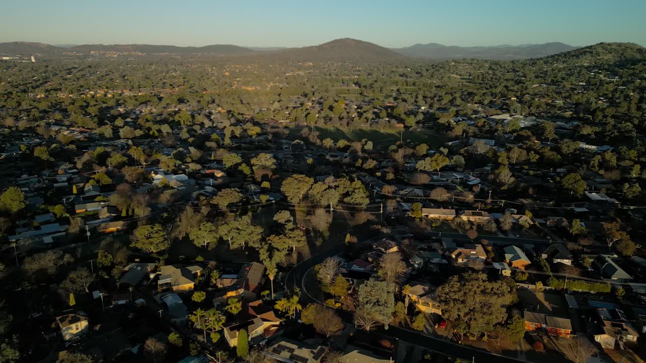 Drone glides sideways over hilly Rivett suburb, showcasing rooftops stretching endlessly into the golden horizon