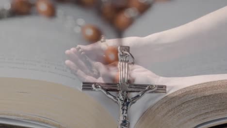 Animation-of-caucasian-woman-praying-with-rosary-over-cross-and-bible