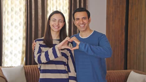 happy indian couple making heart sign with hands