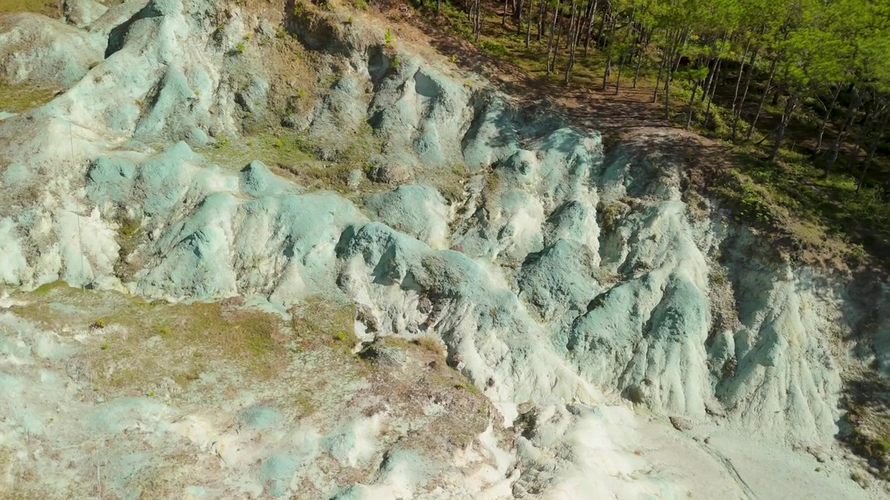 Lähikuva ilmasta paljastaa Sagada Blue Soil Hillsin valkoisen savimuodostelman monimutkaisen uurretun rakenteen, joka hehkuu auringonvalossa mäntymetsän vieressä Mountain Provincessa, Filippiineillä.