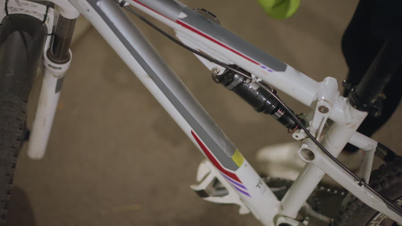 Closeup Of Rider Checking Green Bottle On White Bike Frame, Hand Secures Bottle In Holder, Workshop Glow, Focused On Joints And Bottle Cap, Anticipation Before Night Ride, Textured Tire And Pedal