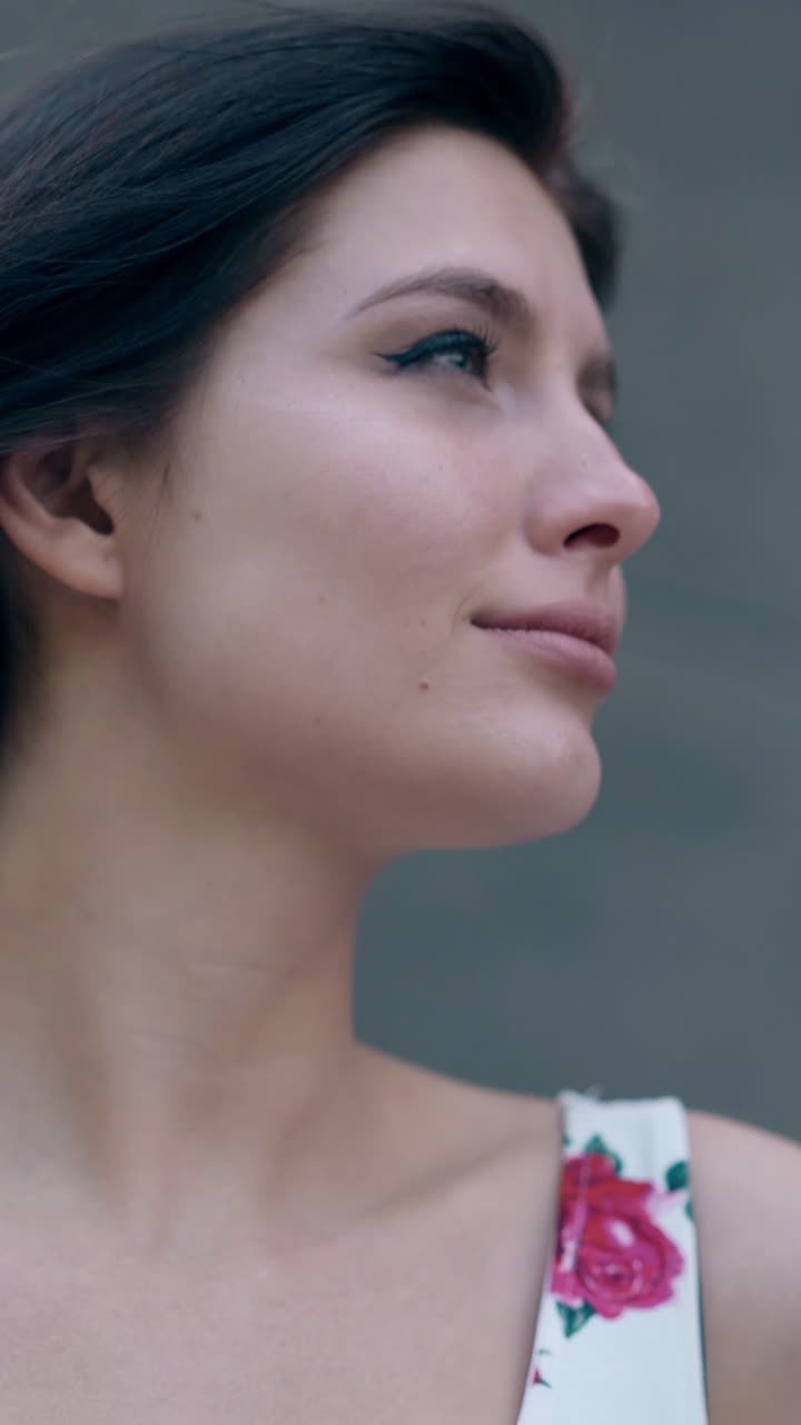 close portrait of beautiful emotional lady with loose flowing dark hair against gray building