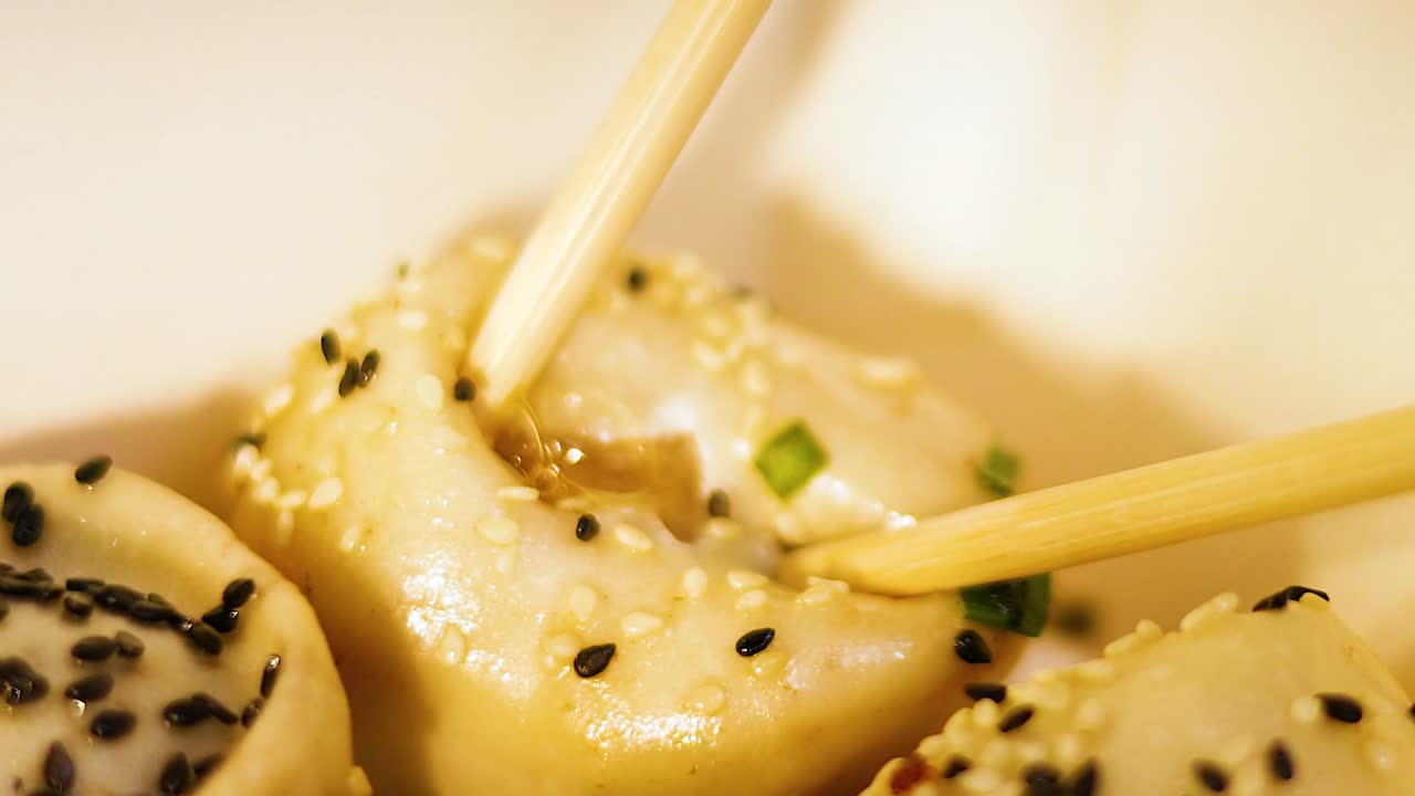 Close-up of chopsticks lifting sesame-seed garnished dumplings with green onion bits.