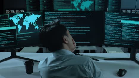 back view of tired asian man developer yawning before sleeping while write code with multiple computer screens in the office