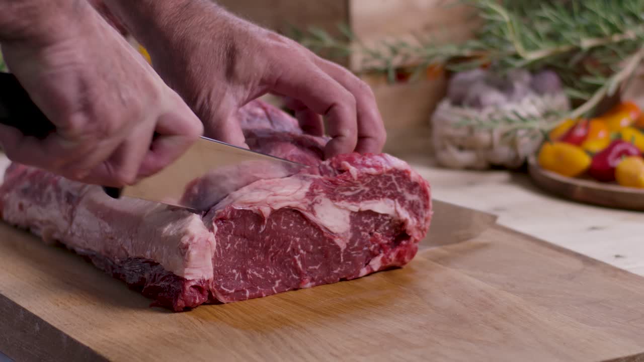Close up of a butcher slicing a fresh marbled ribeye steak from a large beef roast on a wooden cutting board in a kitchen