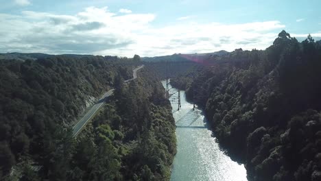 vista aérea, volando sobre una carretera y un río hacia un puente abandonado en un día soleado en nueva zelanda, dolly shot