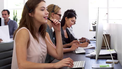 tres mujeres con auriculares trabajando en computadoras en la oficina