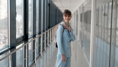 Stylish-young-girl-in-a-blue-business-suit-with-a-handbag-posing-in-front-of-the-camera-in-a-glass-hallway