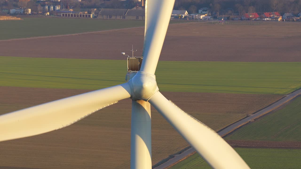 Ripresa aerea ravvicinata di una grande turbina eolica con le sue pale massicce in rotazione. Sullo sfondo è visibile la pittoresca campagna europea con campi e villaggi.