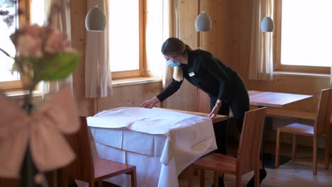 the waitress with a face mask takes the tablecloth from the table