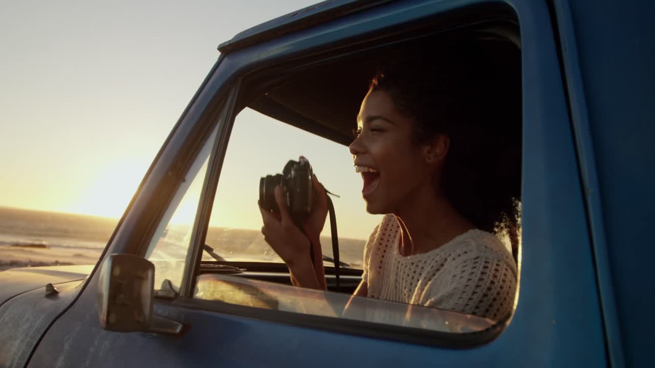 mujer tomando una foto con una cámara digital en una camioneta en la playa 4k