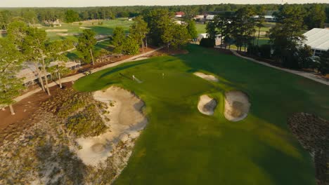 aerial drone shot of a greenskeeper watering the green on a golf hole during sunrise