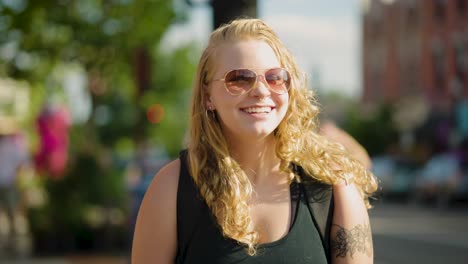 chica con gafas de sol sonríe a la cámara mientras camina por un cruce peatonal en el centro