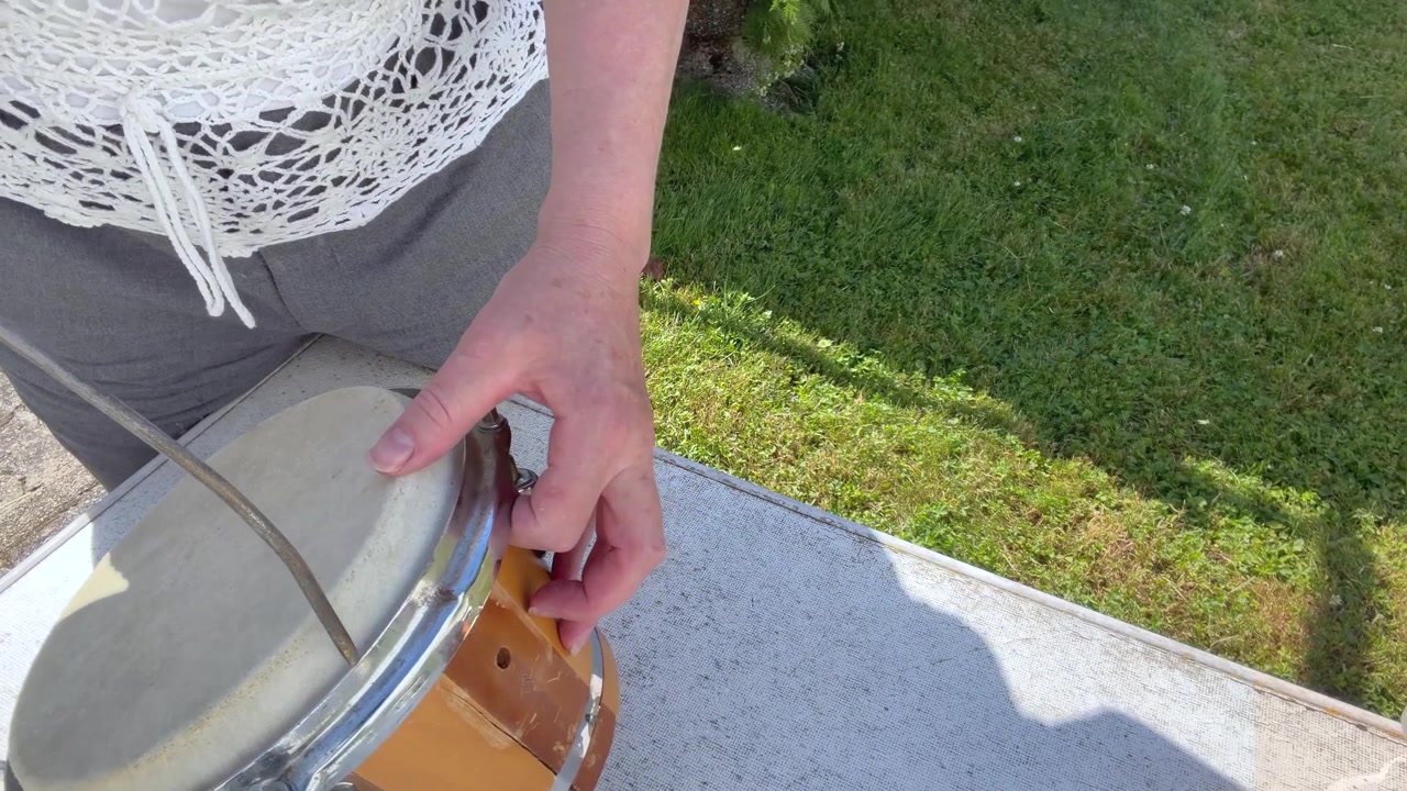 Un primo piano mostra un tamburo a mano tradizionale artigianale pulito con aria compressa. La polvere sottile si solleva. Scatto statico ravvicinato.