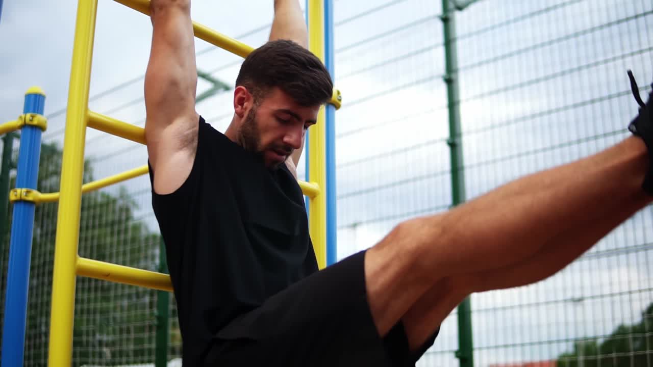 hombre atlético entrenando los músculos del núcleo con levantamiento de piernas en un estante de escalera vertical en un centro de gimnasio al aire libre