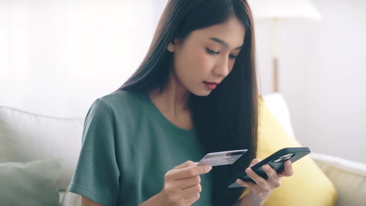 幸せそうな若いアジア人女性が自宅でクレジットカードを持ち、スマートフォンで即時モバイル決済を利用。キャッシュバックを受け取る買い物客のコンセプト