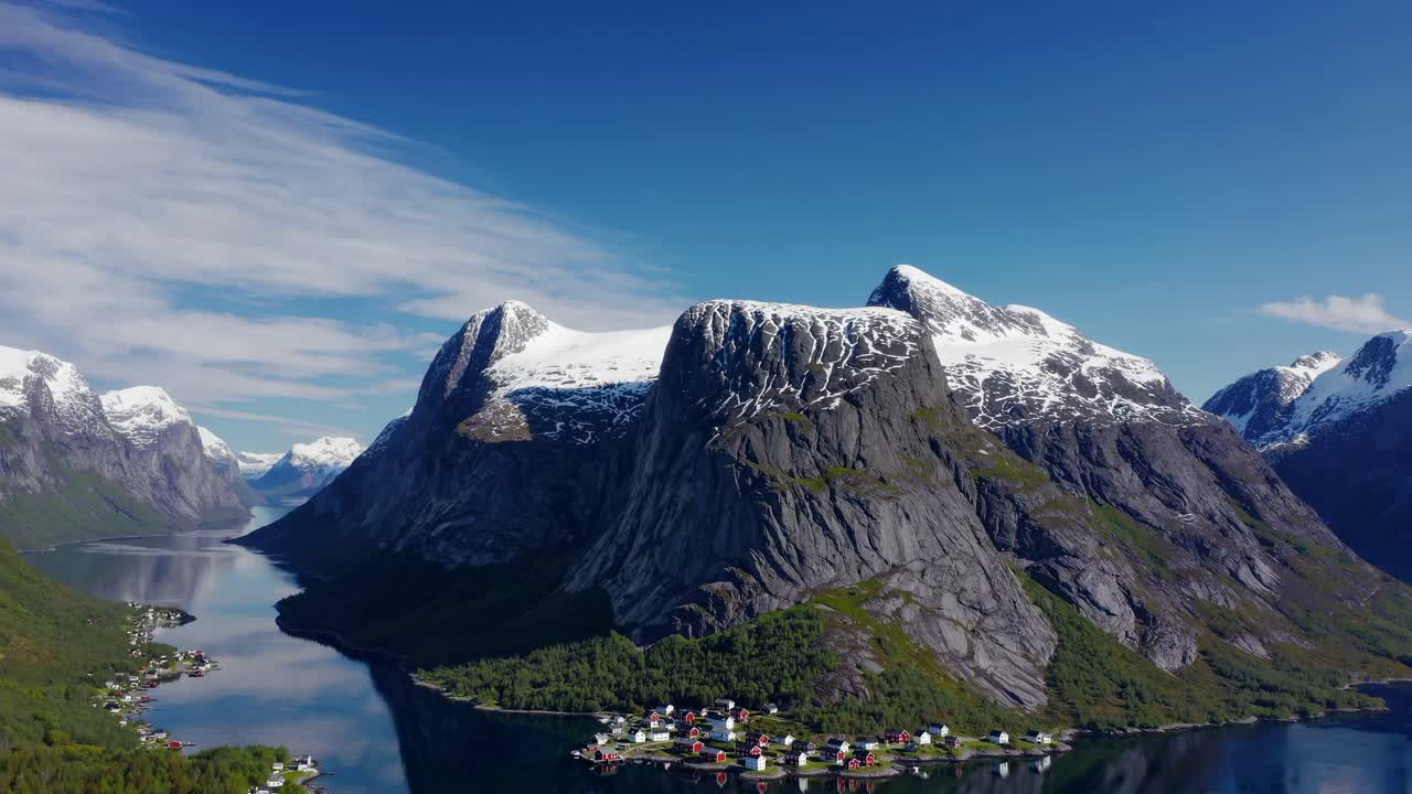 Aerial video captures a scenic village nestled between towering mountains and a serene fjord