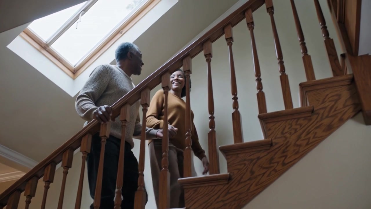 Starting down couple holding hands smiling wood stairs home under skylight, man on rail