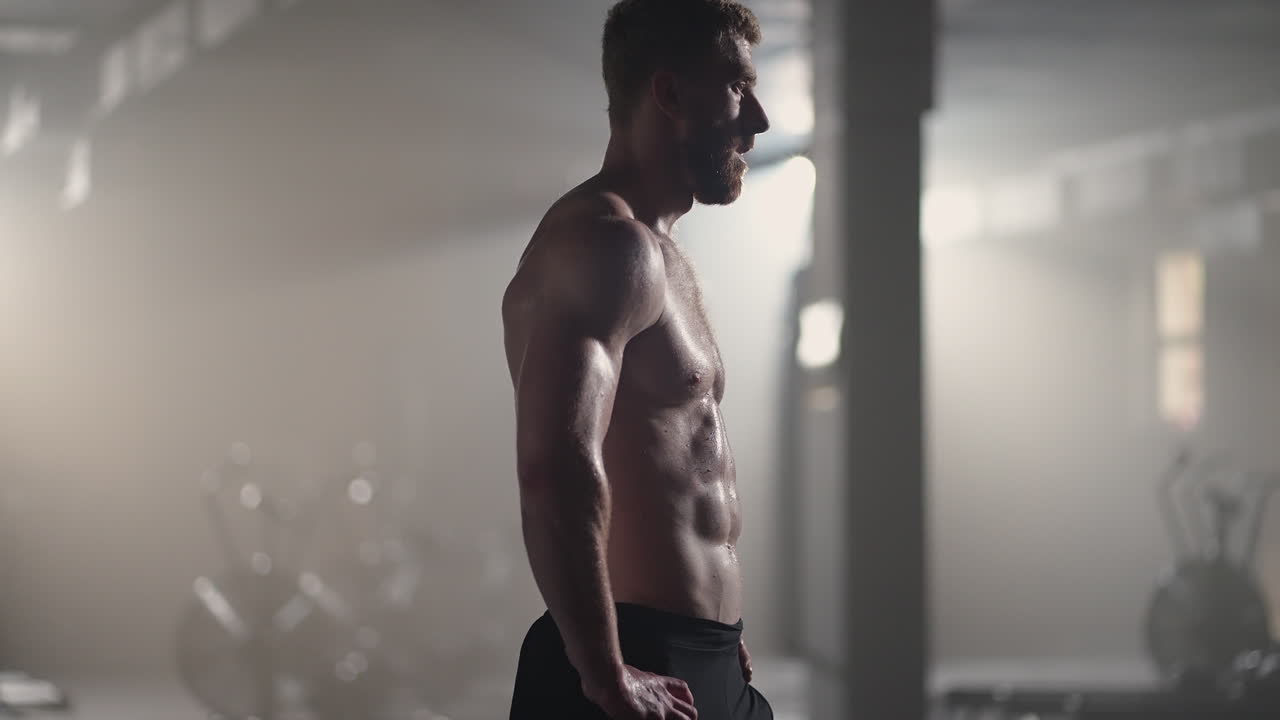 체육관에서 집중적인 운동을 한 후 휴식을 취하는 지친 젊은 남성. 체육관에서 근력 훈련 운동을 한 후 피곤한 건강한 남성. 강렬한 운동을 한 후 서서 휴식을 취하는 피곤한 남성 피트 모델.