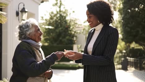 A young woman hands a wrapped gift to an elderly lady outside in a garden. The setting is bright and cheerful, reflecting a warm connection between them.