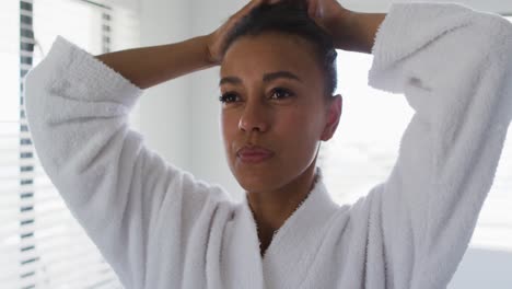 mixed race woman standing in bathroom tying her hair