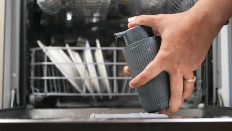 persona que utiliza un dispensador de jabón gris en un lavador de platos