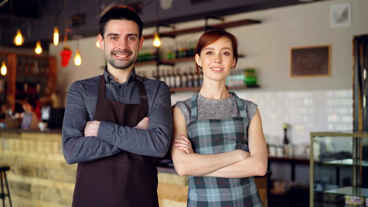 felices y guapos camareros están de pie dentro del nuevo café con las manos cruzadas, riendo y mirando a la cámara. gente hermosa y concepto de servicio de comida.