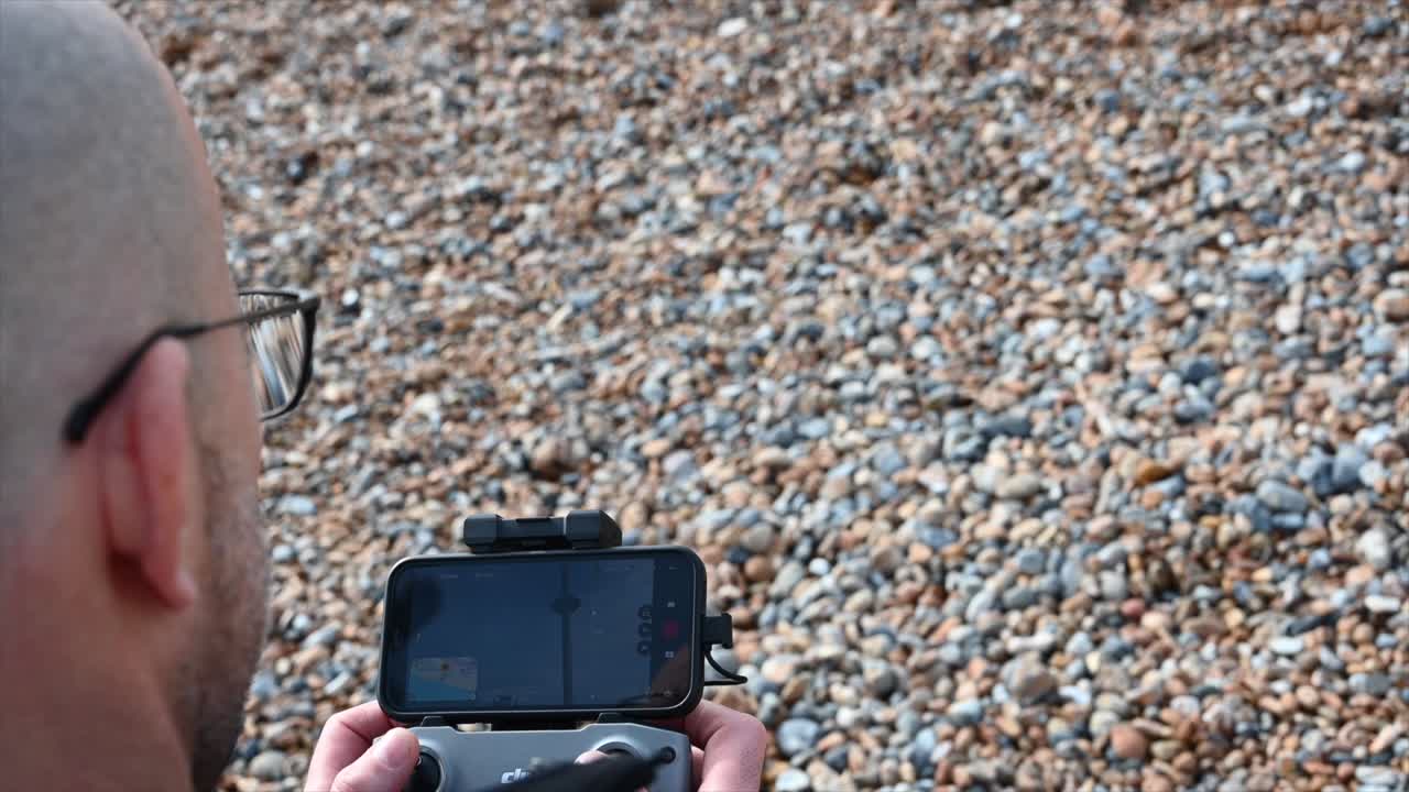 un hombre que usa vidrio está en una playa, brighton, reino unido y está pilotando un dron
