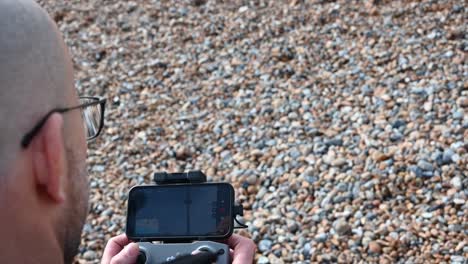 a man who wears glass is on a beach, brighton, united kingdom and he is piloting a drone