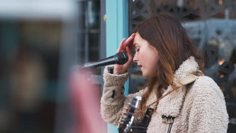 person filming female musician busking playing acoustic guitar and singing to crowd on mobile phone