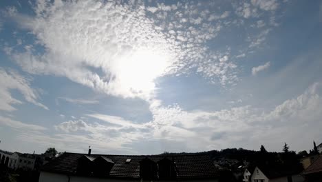 time-lapse of the clouds and the sun setting in a blue sky with some houses in the landscape.