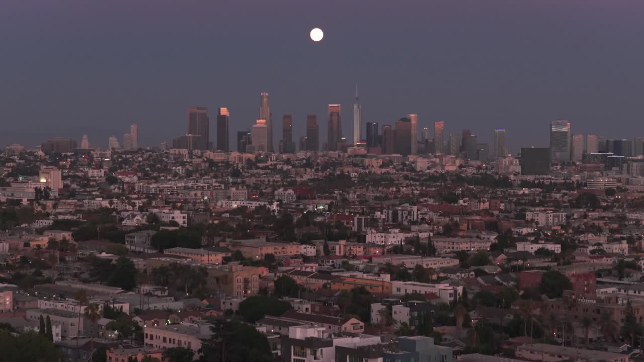 Wide tilting up aerial shot of the of the downtown Los Angeles skyline at sunset during a full buck moon in Southern California. 4K
