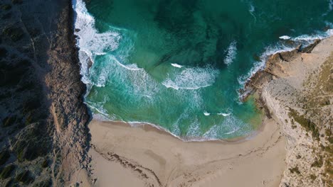 Bird-top-view-beach-bay-with-waves,-clear-turquoise-sea-water,-green-hills,-white-sand