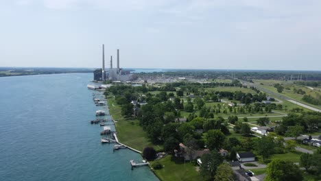 Private-luxury-estates-with-green-gardens-and-massive-power-plant-in-background,-aerial-view