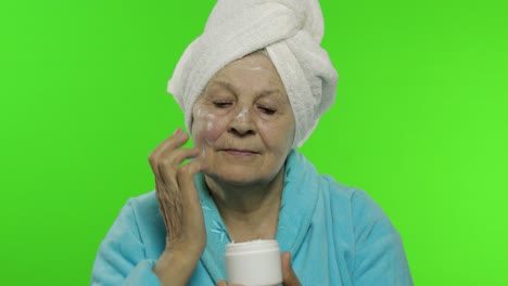 abuela anciana en bata de baño. anciana aplicando crema hidratante en la cara